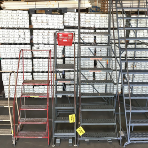 Multiple metal Rolling Ladders sitting side by side on a warehouse floor