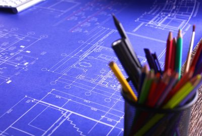 A set of blueprints spread out on a table with pencils and markers in a pencil holder in the foreground of the photo to illustrate warehouse design and consulting services.