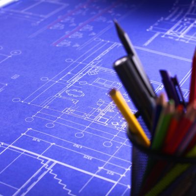 A set of blueprints spread out on a table with pencils and markers in a pencil holder in the foreground of the photo to illustrate warehouse design and consulting services.