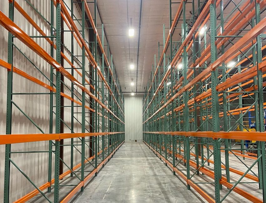 The center aisle of an expansive warehouse featuring orange and green shelving and racking, designed for efficient storage and organization.