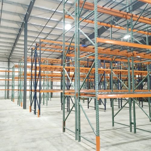 An expansive warehouse featuring multiple shelves and racks in orange and green, designed for efficient storage and organization.